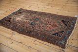 Corner of vintage Persian Mehreban rug showing tattered fringe and worn red, navy pile.