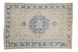 Distressed vintage Oushak carpet, a scalloped royal blue medallion on a soft beige field.