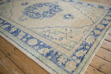 Vintage distressed Oushak rug corner, revealing pale cobalt blue border and worn beige field.