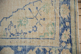 Worn beige Oushak carpet corner, pale cobalt blue and seafoam green floral designs, intact selvage.
