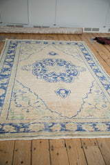 Distressed vintage Turkish Oushak rug corner with beige field and faded blue pattern.