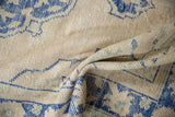 Textured folds of a distressed Oushak rug highlighting worn beige tones and pale cobalt blue designs.