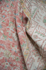 Distressed pile of a vintage Turkish Sparta carpet with faded blush, ivory, and pale green florals.