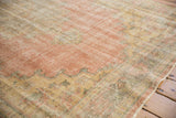 Distressed vintage Oushak rug surface with rose, saffron yellow, and sage green hues.