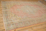 Angled view of distressed vintage Oushak rug, showing worn rose field and faded saffron designs.