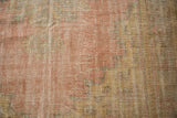Distressed Oushak carpet pile shows worn rose, saffron, and sage tones.