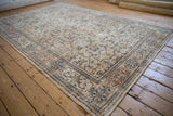 Distressed Oushak carpet showing worn beige, sky blue, and brown stylized patterns.