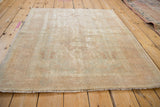 Distressed corner of a vintage Oushak rug, showing faded ivory and rose tones, worn pile, and fringe.