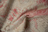 Distressed vintage Oushak rug texture with soft cream and faded dusty raspberry colors.