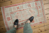 Distressed hand-knotted vintage Oushak rug corner with ivory, sea foam, and tangerine floral border.