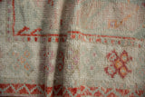 Distressed vintage Oushak rug pile, folded, with time-softened ivory, coral, and pale green tones.