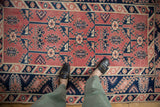 Distressed vintage Melas rug displaying cherry red, navy, ivory tribal geometric motifs.