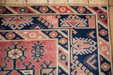 Distressed Melas rug corner showcasing navy, cherry red hook and latch motifs and fringe.