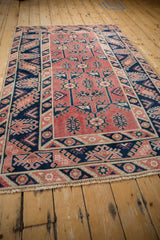 Distressed Turkish Melas rug corner, showing pale cherry red, navy, and ivory hook and latch motifs.