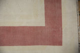 Distressed vintage Oushak rug corner, displaying ivory field, faded raspberry border, and fringed edge.