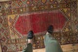 Feet on distressed cherry red vintage Anatolian rug with geometric saffron yellow borders.