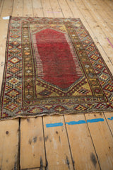 Distressed Anatolian rug corner: cherry red field with wear, hook and latch spandrel, geometric borders.