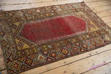 Vintage distressed Anatolian rug corner showing cherry red field, hook and latch motifs.