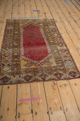 Distressed Anatolian rug corner with cherry red field, hook and latch spandrels, and geometric borders.