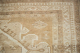 Distressed Oushak rug corner with geometric border patterns and warm neutral abrashes.