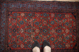 Worn cherry red pile and blue Herati design of a vintage Malayer rug with feet.