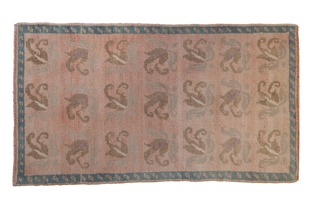 Vintage distressed Oushak rug with rows of floral tendrils in muted silver and beige on a dusty rose field with a turquoise blue border.