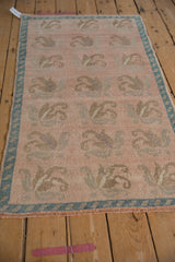 Angled view of a distressed Oushak rug showing its floral pattern and dusty rose palette.