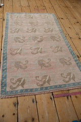 Angled perspective of a distressed Oushak rug with a pale rose field and turquoise border.