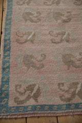 Softly worn pile of a vintage Oushak rug with floral tendrils on a dusty rose field beside a teal border.