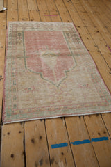 Angled perspective of a vintage Oushak prayer rug with dusty pink and sea foam green tones.