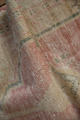 Softly folded vintage Oushak rug showing a distressed texture in dusty pink and cream.