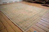 Distressed Oushak carpet corner, displaying worn texture and faded peach, green, and blue.