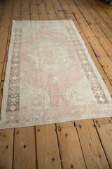 Distressed Oushak rug's corner with worn pale pink field and starburst motif border.