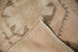 Textured beige and charcoal distressed Kurd rug pile with exposed foundation and cording.