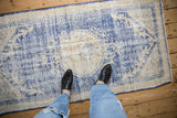Distressed Oushak rug showing worn pile and faded cobalt blue and cream roundel pattern.