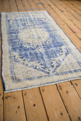 Distressed Oushak rug corner with faded cobalt blue and cream pattern, visible wear, and intact selvage.