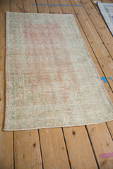 Faded dusty rose, ivory, and mint green tones on the distressed Oushak rug pile.