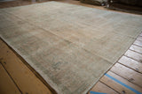 Angled view of a distressed Oushak rug, showing the time-softened patina and low pile in pale sandalwood tones.