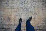 Distressed vintage Oushak carpet showing worn pile, exposed foundation, and faded blue floral motifs.