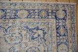 Vintage distressed Oushak corner with textured pile, showing pale sandalwood and deep blue design.