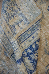 Distressed Oushak carpet detail: sand, cobalt blue, worn pile, and visible foundation.