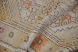 Textured, distressed pile of vintage Oushak rug showing ivory, brown, and tangerine geometric motifs.