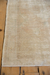 Close-up of distressed Oushak rug, showing worn beige pile, side selvage, and faint seafoam.