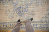 A person's perspective highlighting the distressed texture and low pile of a vintage Oushak carpet.