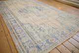 Angled corner view of a distressed Oushak carpet showing the worn pile and pale blue palmette border.