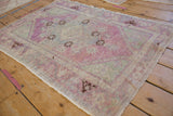 Angled view of a distressed Turkish Oushak rug showing its worn texture and faded purple palette.