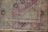 Detail of a distressed Oushak rug corner with low pile, exposed foundation, and purple motifs.