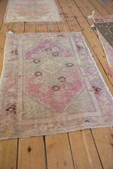 Angled view of a vintage distressed Oushak rug with a faded palette of purple and seafoam green.