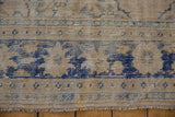 Worn vintage Oushak rug edge showing exposed foundation, pale blue border, and fringe.