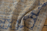 Distressed Oushak carpet pile showing worn cream foundation, pale cobalt blue motifs, and fringe.